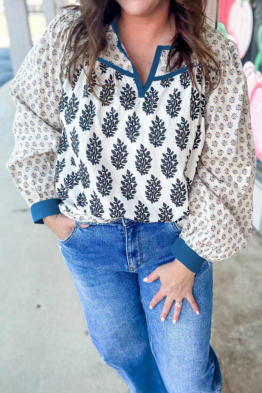 Person wearing a patterned blouse and blue jeans with a blurred background