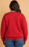Woman shown from behind wearing a bright red crewneck sweatshirt with blue jeans.