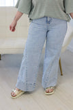 A person wearing light-wash wide-leg denim jeans with rolled cuffs, paired with a green striped top and beige platform sandals, standing in a bright indoor room.