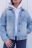 Person wearing light blue polka-dot denim jacket over white hoodie and navy pants against paneled wall.