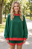 A woman wearing a dark green holiday-themed lounge set with red and white polka dot trim, standing on a paved path in a park.