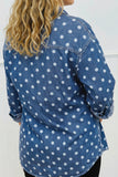 A woman wearing a blue denim shirt with a white polka dot pattern, shown from the back.