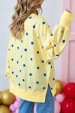 A woman shown from the back wearing a yellow long-sleeve top with blue polka dots, paired with blue jeans, in a decorated indoor setting with balloons.