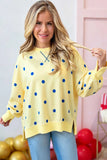 A woman wearing a pale yellow long-sleeve sweatshirt with blue polka dots, paired with light blue jeans, standing in a decorated room with balloons.