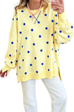 A woman wearing a pale yellow long-sleeve sweatshirt with blue polka dots, paired with white pants and a pink beaded necklace, holding a phone in a mirror selfie.