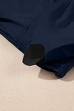 Close-up of a navy blue ribbed fabric garment laid on a textured beige surface, with a black curved trim or accent visible near the lower edge.