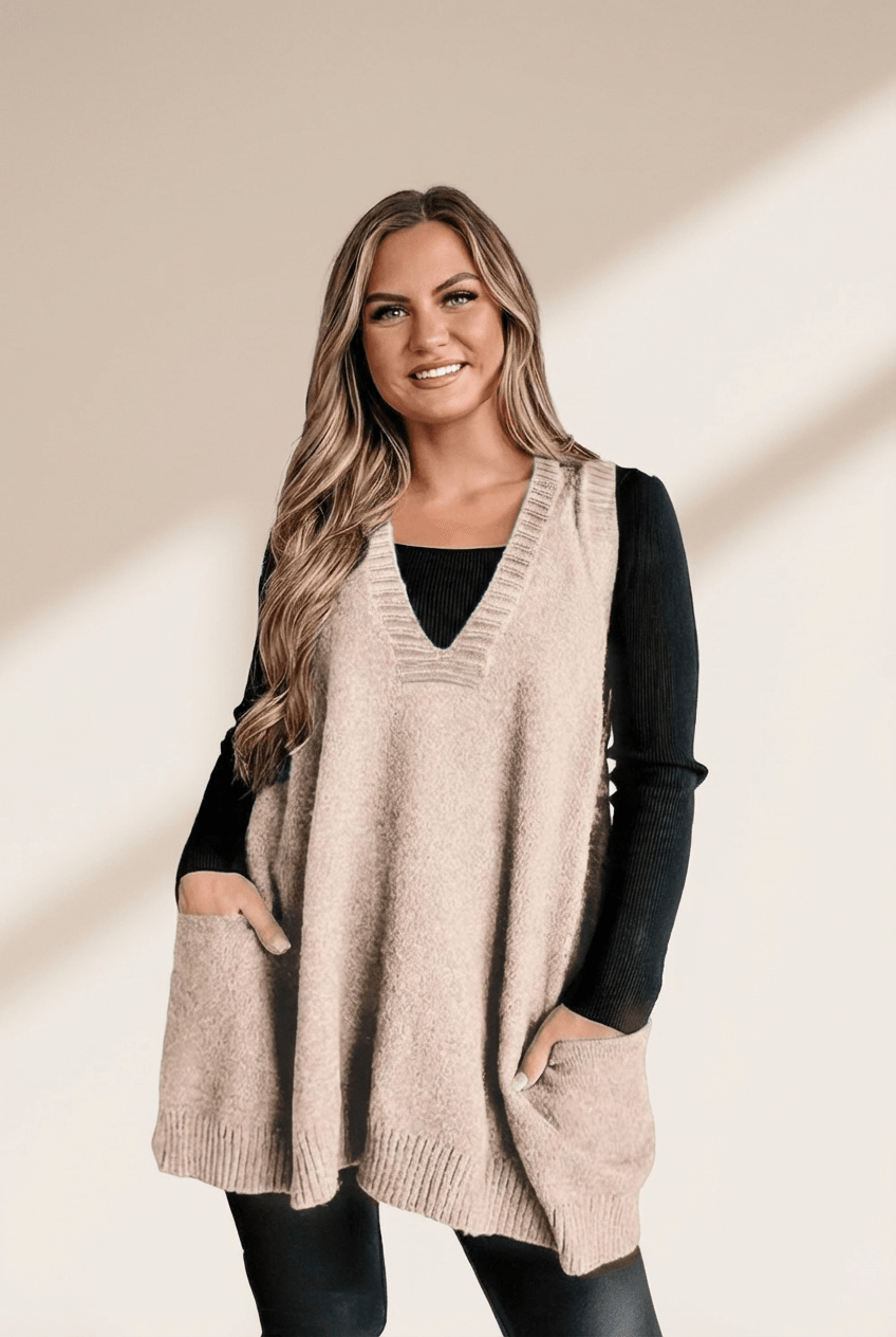 Woman wearing a beige sweater vest over a black long-sleeve shirt on a beige background