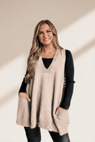 Woman wearing a beige sweater vest over a black long-sleeve shirt on a beige background