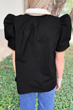 Person wearing a black top with ruffled sleeves and a white collar, standing outdoors.