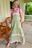 Woman wearing a green floral dress with pink accents on a porch.