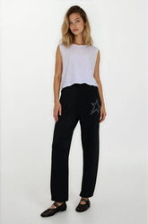 Woman wearing a white sleeveless top and black pants with a star design on a white background