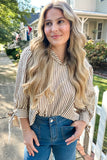 Woman with long blonde hair wearing a striped shirt and blue jeans standing outdoors.