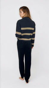 Person wearing a navy sweater with beige stripes and matching pants on a white background