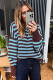 A woman takes a mirror selfie wearing a cozy knit sweater with horizontal stripes in light blue and dark brown, paired with dark blue jeans.