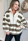 A woman wearing a cream and olive green horizontally striped quarter-zip pullover sweatshirt, paired with black pants, standing against a light-colored wall with hats hanging on the right.