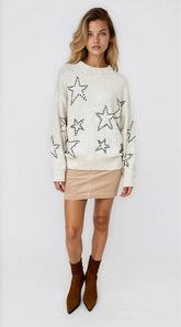Woman wearing a cream sweater with star patterns on a white background