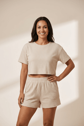 Woman wearing a beige crop top and shorts set against a plain background