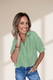 Woman wearing a green striped shirt and blue jeans against a beige background