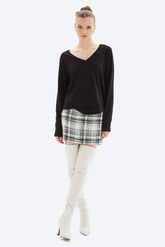 Woman wearing a black long-sleeve top, plaid skirt, and white knee-high boots on a white background