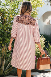 Woman wearing a striped dress with leopard print collar holding a brown handbag in a garden setting.