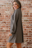 Woman wearing a gray dress standing against a brick wall