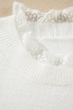 Close-up of a white knit sweater featuring a delicate white lace ruffle trim around the crew neckline, set against a neutral beige background.
