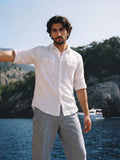 Man in a white shirt and gray pants standing by a body of water with trees in the background