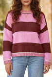A woman wearing a pink and dark brown striped knit sweater with light blue jeans, shown from the chest down against a softly blurred outdoor background.
