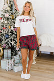 Woman wearing a Merry graphic tee and matching red plaid shorts.