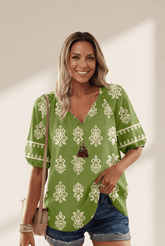 Woman wearing a green patterned blouse with denim shorts against a plain background
