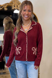 Woman in burgundy zip-up cardigan with beige trim and bow pockets, paired with light blue jeans.
