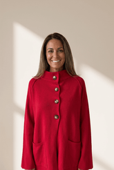 Woman wearing a red coat with silver buttons against a beige background