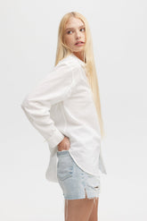 Woman wearing a white blazer over a light blue denim shirt on a white background