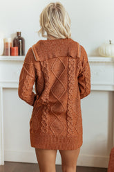 Back view of woman in oversized rust-orange cable-knit sweater near white fireplace mantel.