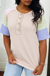 Woman wearing a ribbed knit top with color-blocked sleeves against a neutral background