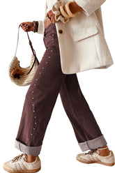 Wide-leg brown pants with silver studs, cream blazer, beige sneakers, and straw bag.