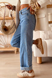 Light blue wide-leg jeans with silver rivets, cream coat, beige sneakers, and straw bag.