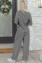Person wearing a black and white checkered outfit standing in front of a stone wall.