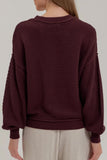 Back view of woman in deep burgundy waffle-knit sweater with light beige trousers.