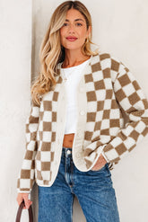 Woman in a checkered cardigan, white shirt, and blue jeans against a plain background.