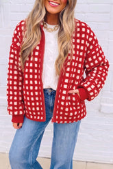 Woman in red-white fuzzy checkered cardigan, cable-knit top, and blue jeans by white brick.