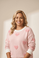 Woman wearing a pink sweater with heart patterns against a plain background