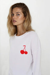 Woman wearing a white sweatshirt with red cherry design on a plain background