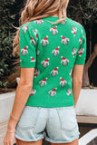 Back view of woman in bright green sheep-print sweater with red Santa hats and denim shorts.