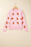 Pink knit sweater with gingerbread pattern and colorful details on wooden hanger.