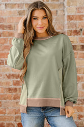 Woman wearing a green sweater with brown trim against a brick wall