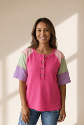 Woman wearing a pink and multicolored top against a beige wall