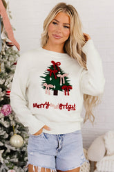 Woman in cream Christmas sweater with green tree, red bows, and 'Merry and Bright' text with denim shorts.