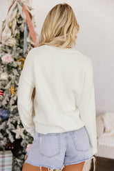 A woman viewed from behind wearing an off-white crewneck sweatshirt and light-wash denim shorts.