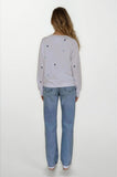 Person wearing a light gray sweatshirt with star patterns and blue jeans on a white background